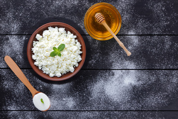 Cottage cheese in clay bowl and honey on wooden boards. Sour cream in wooden spoon. Dairy products and honey on dark background. Fresh mint and soft cheese for breakfast