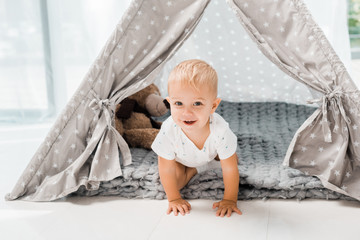 smiling adorable toddler sitting in baby wigwam with fluffy teddy bear toy © LIGHTFIELD STUDIOS