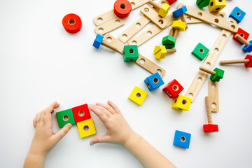 Obraz premium Close up of child hands playing with colorful wooden bricks at the table. Toddler having fun and building out of bright constructor bricks. Early learning. Top view. Flat lay.