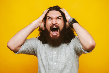Bearded man screaming over yellow background