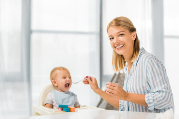 happy mom feeding son in highchair with baby food