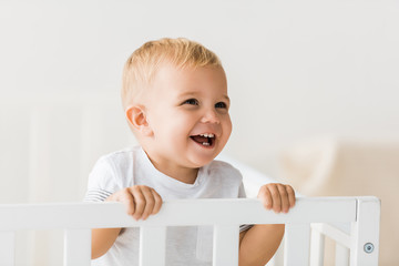 cheerful toddler standing in baby crib on white background - obrazy, fototapety, plakaty