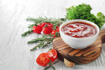 Tasty tomato sauce in bowl with herbs on white wooden table