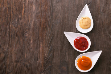 Plates with different tasty sauces on wooden table