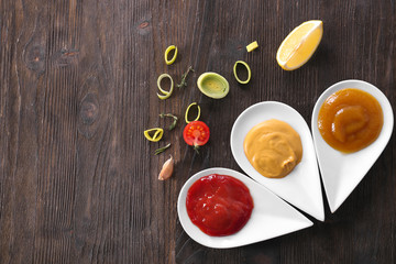 Plates with different tasty sauces on wooden table