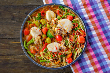Som Tam Seafood (Spicy Papaya Salad) with salted squid, on wooden table ( Thai food)