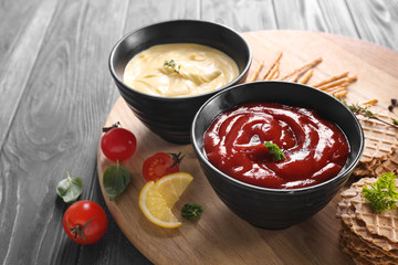 Tasty sauces in bowls with snacks on wooden board