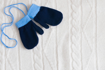 Pair of blue knitted mittens on a white woolen fabric.