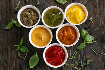 Different tasty sauces in bowls with herbs on wooden table