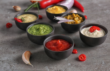 Different tasty sauces in bowls on grey table