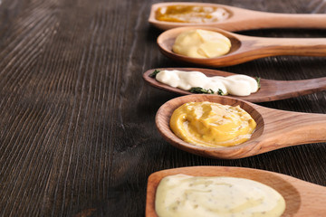 Spoons with tasty sauces on wooden table