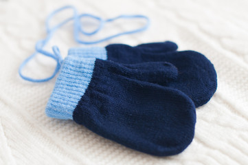 Pair of blue knitted mittens on a white woolen fabric.