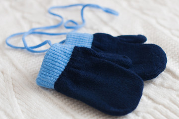 Pair of blue knitted mittens on a white woolen fabric.