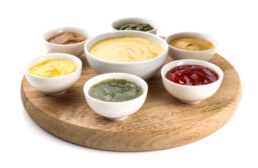 Wooden board with tasty sauces in bowls on white background