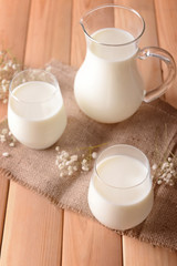 Composition with glasses and jug of tasty milk on wooden table