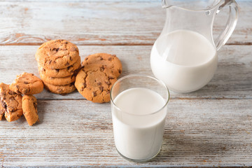 Cookies, glass and jug of tasty milk on wooden table