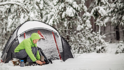 Happy woman cooking near winter tent camp in the snow forest.