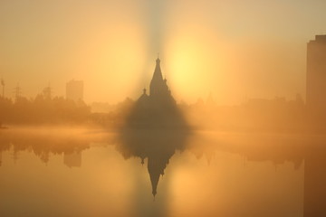 Sunrise near the church, city background. Foggy morning. the mist over the water. skyscrapers around the old building