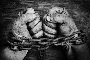 Powerful dirty male hands clenched into fists chained with rusty chain. Black and white photo.