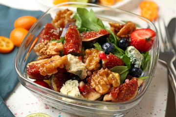 Delicious fresh salad with walnuts in glass bowl on light table