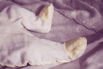 Baby feet in yellow romper on the blanket, close-up
