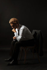 Thoughtful businessman sitting on chair against black background