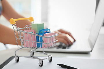 Small cart on table of woman using laptop. Internet shopping concept