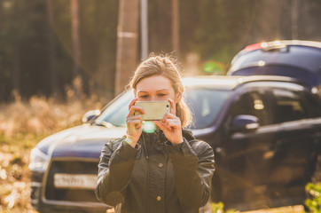 Woman with smartphone posing on against car while stopping while traveling