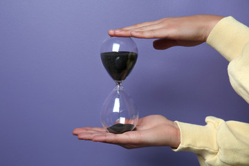 Female hands holding hourglass on color background