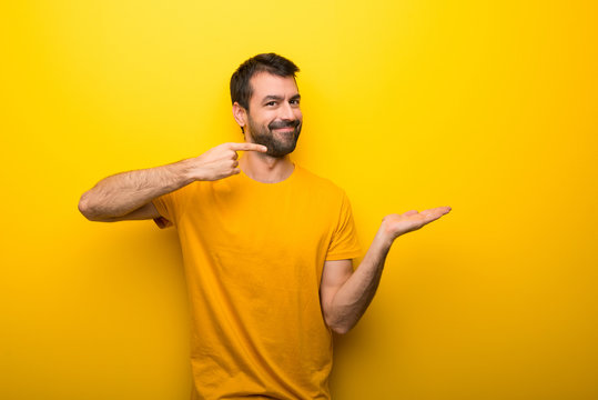 Man on isolated vibrant yellow color holding copyspace imaginary on the palm to insert an ad
