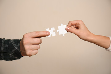 Fototapeta premium Male and female hands with pieces of puzzle on light background