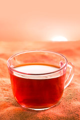 Glass cup of tea on the sand on sunset bacground. Cup of tea on wilderness.