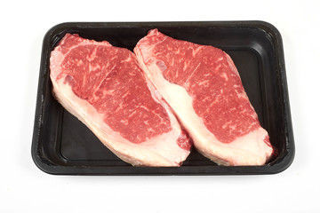 Raw sirloin beef steak in plastic packaging tray.