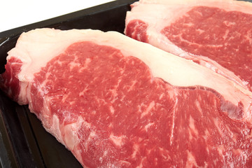 Raw sirloin beef steak in plastic packaging tray.