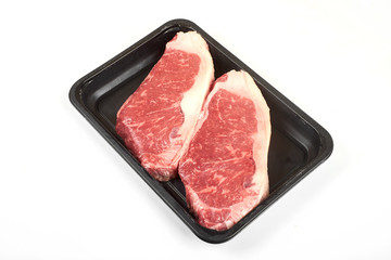 Raw sirloin beef steak in plastic packaging tray.