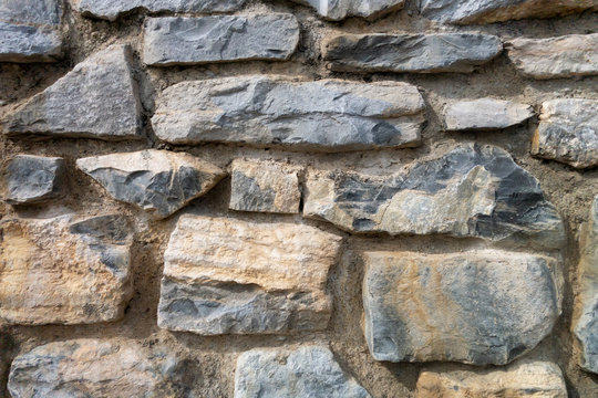 The wall, built of a mixture of large stones of various shapes and cement. Background, texture, black, yellow and gray rocks, close up
