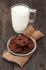 Glass cup of milk and chocolate cookies on a dark wooden background