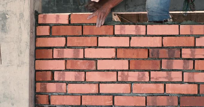 Asian man laying bricks on top of mortar to build brick wall