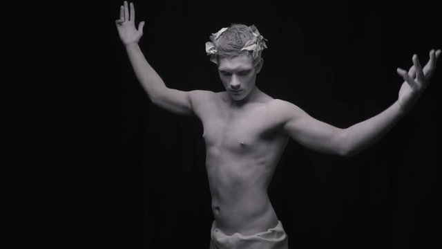 Young fit man as a statue spreads his arms and bends over