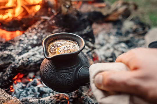 Boiling coffee in turkish cezva on campfire coals. Luxury camping concept.
