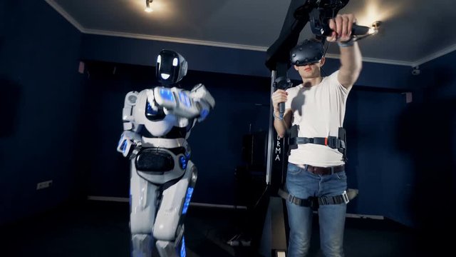 Human-like robot and a teenage guy in VR goggles are throwing hands forward together