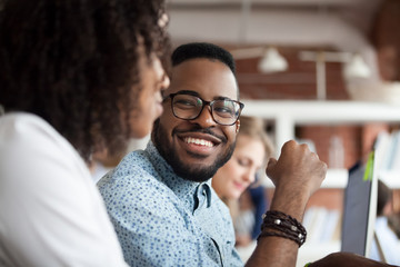 Close up of smiling African American employee look at female colleague chatting in office, happy black male worker talk with woman coworker, having casual conversation at workplace, have fun