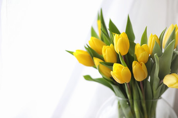 A bouquet of yellow tulips in a vase on the windowsill. A gift to a woman's day from yellow tulip flowers. Beautiful yellow flowers in a vase by window.