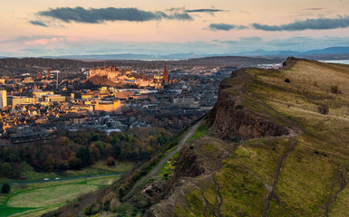 View of the Salisbury Crags from Arthur's Seat at sunrise, with the sun shining on Edinburgh's Castle in the background. Edinburgh, Scotland.  Landscape. Cityscape. Travel.