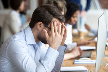 Nervous male employee massage temples worry to finish work till deadline, stressed worker sit in...