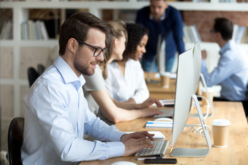 Happy male employee working at computer typing business email or chatting with friends, smiling man...