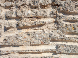 A wall made of small stones of various rocks and cement with yellow sand. There are horizontal long grooves in the wall, background macro