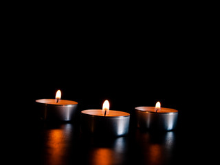 Obraz na płótnie Canvas Three lighted candles with an orange flame and isolated on a black background