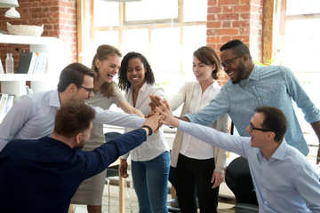 Excited multiracial colleagues give high five involved in teambuilding activity at meeting, happy...
