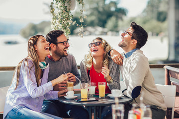 Group of four friends having fun a coffee together. Two women and two men at cafe talking laughing and enjoying their time